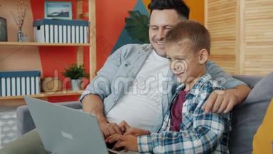 父子俩一起坐在沙发上用笔记本电脑聊天